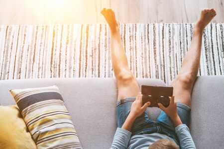 Boy sits on sofa plays with smartphone and gamepad camera top view. Child and electronic devices conceptの写真素材