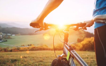 Man hands on the bike steering wheel close up image. Man with bike stay on the top of hill and enjoying the sunset.の写真素材