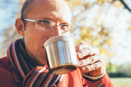 Man in Eyeglasses with cup of hot drink warming on open autumn air in the parkの写真素材