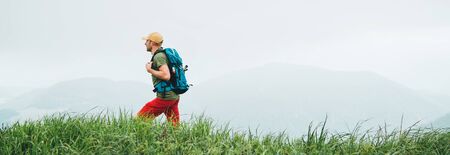 Side shot of hiker man walking by the foggy cloudy weather mountain range path with backpack. Active sport backpacking healthy lifestyle concept. Website header cropping.の写真素材