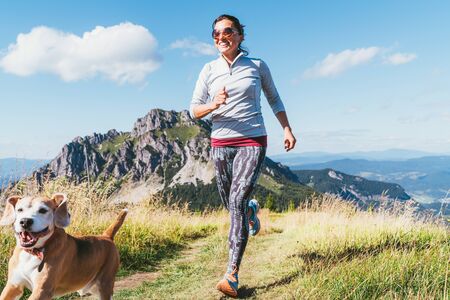Happy smiling female jogging by the mounting range path with her beagle dog. Canicross running healthy lifestyle concept image.の写真素材