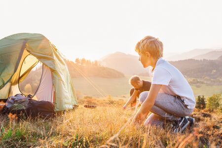 Father and son setting camping tent on the sunset mountain valley at the eveningの写真素材