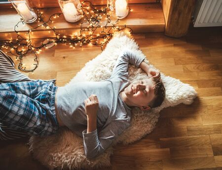 Boy lying on floor on sheepskin and looking in window in cozy home atmosphere. Peaceful moments of cozy home concept image.の写真素材