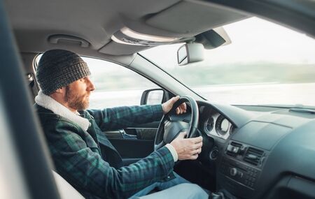 Warm dressed Bearded Man driving a new modern auto. Inside car view.の写真素材