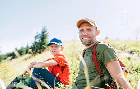 Smiling Father and teenager son portrait sitting on the grass during their mounting hiking walking.の写真素材
