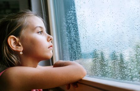 Little sad girl pensive looking through the window glass with a lot of raindrops. Sadness childhood concept image.の写真素材