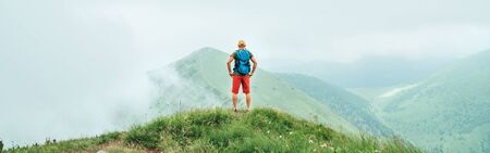 Hiker man walking by the cloudy and foggy weather mountain range path with backpack. Active sport backpacking healthy lifestyle concept.の写真素材