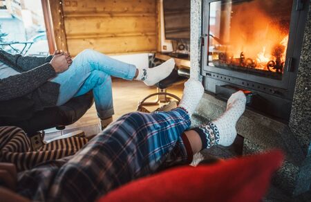 Father with son sitting in comfortable armchairs in their cozy country house near fireplace and enjoying a warm atmosphere and flame moves. Parents and kids time spending concept image.の写真素材