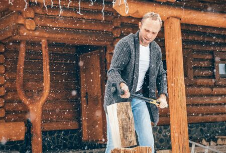 Man chopping wood on snowy yard for a house fireplace with heavy snowflakes background . Winter countryside holidays concept imageの写真素材