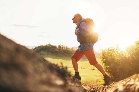 Backpacker traveler in trekking boots jumping over the ditch on mountain dirty path at summertime sunny day side shot image.の写真素材