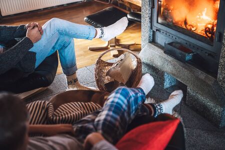 Father with son sitting in comfortable armchairs in their cozy country house near fireplace and enjoying a warm atmosphere and flame moves.の写真素材