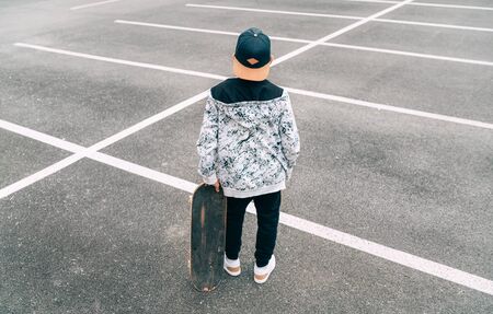 Teenager skateboarder boy with a skateboard standing on asphalt playground and resting after he made tricks.の写真素材