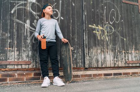 Teenager skateboarder boy standing beside a wooden grunge graffiti wall with skateboard and Water bottle flask.の写真素材