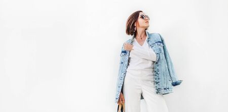 Posing woman in elegant white outfit with oversize denim jacketの写真素材
