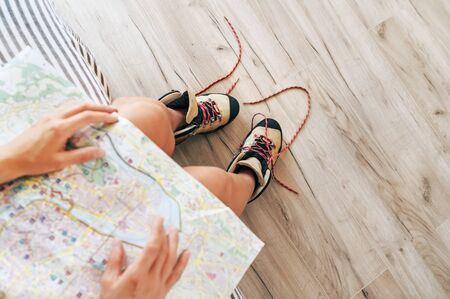 Young female inspecting a city map resting on the bed with untied trekking boots on wooden floorの写真素材