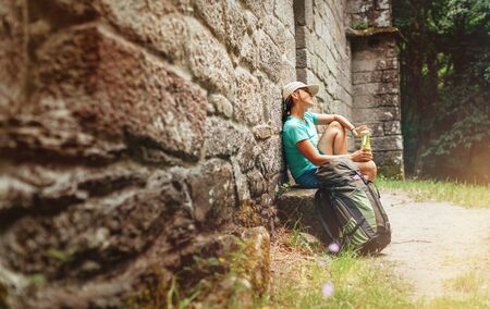 Tired female backpacker resting on the bench near the old antique brick wall castle on the famous Camino de Santiago way.の写真素材