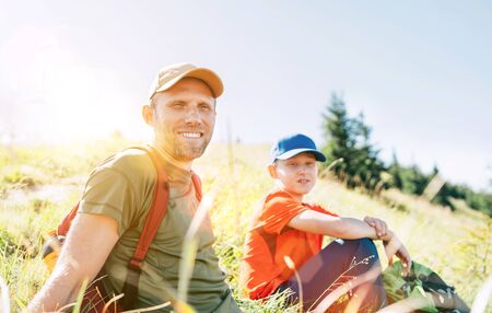 Smiling Father and teenager son portrait sitting on the grass during their mounting hiking walking.の写真素材