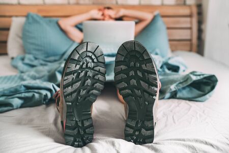 All time ready for trekking. Hiker was sleeping in comfort trekking boots and now she browsing an internet using a laptop and lazily stretching after sleeping.の写真素材