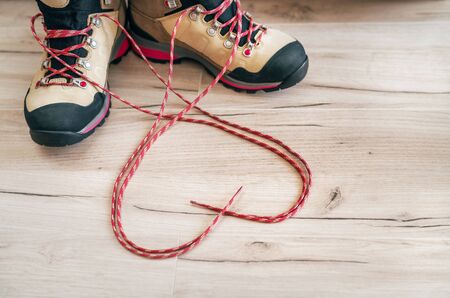 Conceptual image of the pair new trekking boots on the wooden floor  with released long shoelaces behind lying in heart shape.の写真素材