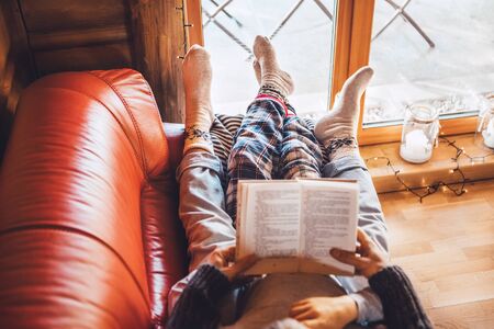 Father and son reading book together lying on the cozy sofa in warm country house.の写真素材