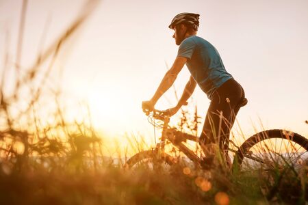 Man biker man meets a sunset in top of hill over the city.の写真素材