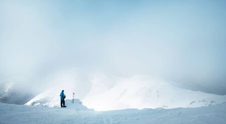 Winter Trekker staying on mountain peak he climbed and enjojing wide panorame view of valley covered by storm clouds. Active winter trekking concept image.の写真素材