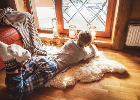 Boring boy lies on the floor and look sout from window in cozy and warm livivng roomの写真素材