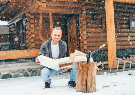 Man chopping wood on snowy yard for a house fireplace with heavy snowflakes background . Winter countryside holidays concept imageの写真素材