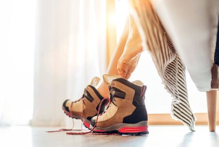 Young sexy barefoot female putting on a New trekking boots with untying laces under the bad view in...