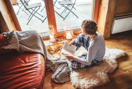 Boy reading book on the floor on sheepskin in cozy home atmosphere. Peaceful moments of cozy home concept image.の写真素材