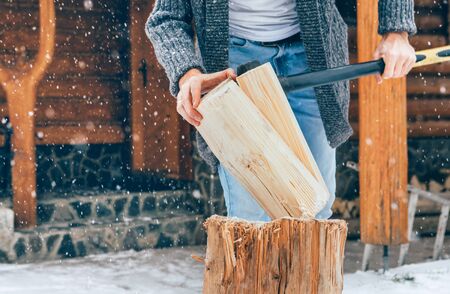 Man chopping wood on snowy yard for a house fireplace with heavy snowflakes background . Winter countryside holidays concept imageの写真素材