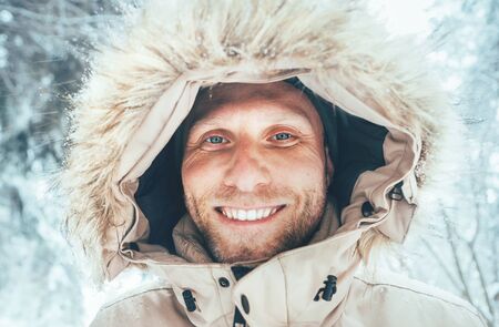 Man dressed in Warm Hooded Casual Parka Jacket Outerwear walking in snowy forest cheerful smiling face portrait. Outdoor time and winter outfit concept image.の写真素材