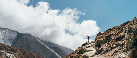Hiker man silhouette on clouds background standing on path going over the Imja Khola valley during...