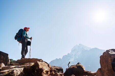 Young hiker backpacker female on cliff edge enjoying the Thamserku 6608m mountain during high altitude Acclimatization walk. Everest Base Camp trekking route, Nepal. Active vacations concept imageの写真素材