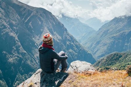 Young hiker backpacker sitting on the peak edge and enjoying mountains view valley during high altitude Everest Base Camp (EBC) trekking route near Phortse, Nepal.の写真素材