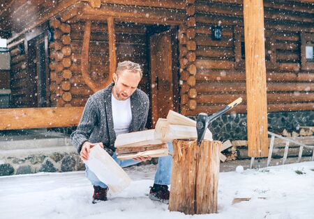 Man chopping wood on snowy yard for a house fireplace with heavy snowflakes background . Winter countryside holidays concept imageの写真素材