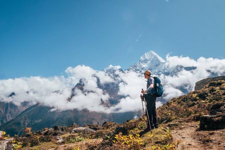 Young hiker backpacker man using trekking poles enjoying the Thamserku 6608m mountain during high altitude Acclimatization walk. Everest Base Camp trekking route, Nepal. Active vacations concept imageの写真素材