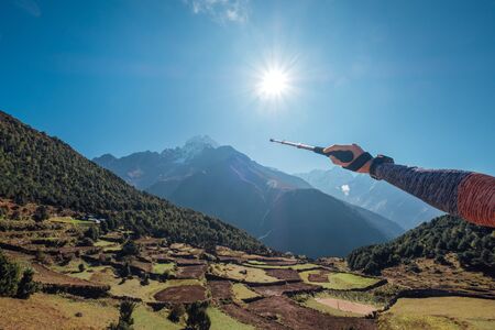 Hiker backpacker man using trekking poles showing on Thamserku 6608m mountain during high altitude Acclimatization walk. Everest Base Camp trekking route, Nepal. Active vacations concept imageの写真素材