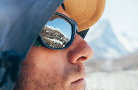 Portrait shot of high altitude unshaven happy mountain hiker in baseball cap and hood with snow peaks and mountainの写真素材