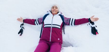 Young smiling female liying on the white snow wide opened her arms.の写真素材