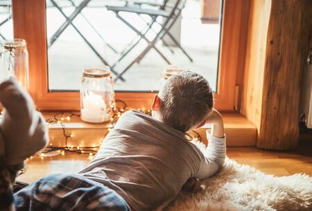 Boy lying on floor on sheepskin and looking in window, lost in dreams or boring.の写真素材