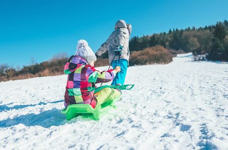 Little boy carrying girl in the sled and enjoying winter sledding time. Funny winter holidays spending concept image.の写真素材