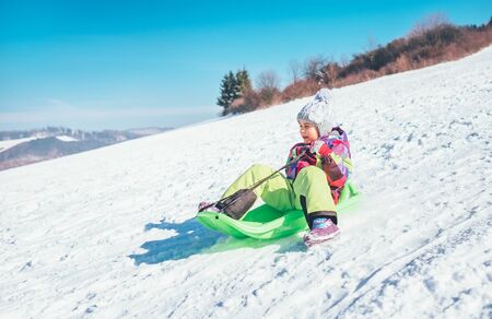 Happy laughing little girl sliding down from the snow slope. Funny winter holidays spending concept image.の写真素材