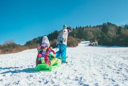 Little boy carrying girl in the sled and enjoying winter sledding time.の写真素材