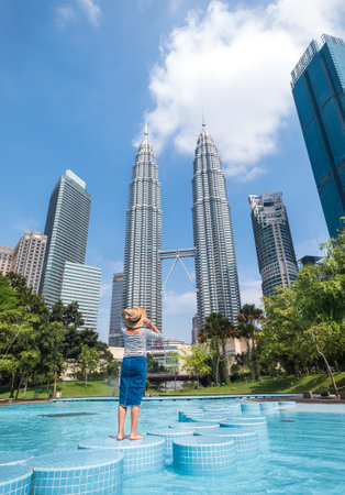 Kuala Lumpur city, Malaysia â MARCH 12, 2019: Young female tourist in straw hat enjoying of two Petronas Towers skyscrapers in Kuala Lumpur city center, Malaysiaのeditorial素材