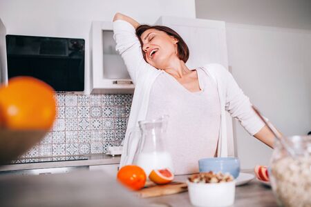 Beautiful young woman stretching after awakening and yawning at modern kitchen.の写真素材