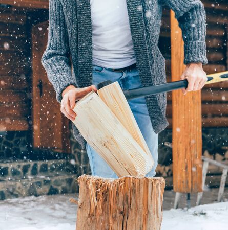 Man chopping wood on snowy yard for a house fireplace with heavy snowflakesの写真素材