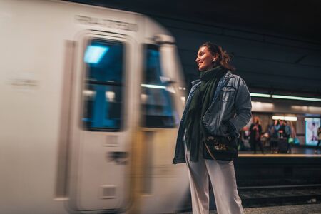 Elegant woman dressed in oversize denim jacket and wide white trousers waiting for a subway trainの写真素材