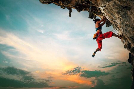 Athletic Woman climbing on overhanging cliff rock with sunset skyの写真素材