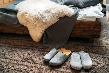 The two pair of gray home slippers near the wooden bed on the "knitted floor" in the cozy bedroom.の写真素材